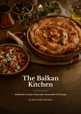 A rustic food photography cover for 'The Balkan Kitchen' by Just Cook It kitchen, featuring a golden-brown baked pastry in a round wooden dish on a dark wooden table, surrounded by bowls of food and herbs.