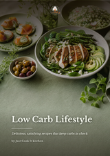 A styled food scene on a muted green surface showing a bowl of sliced grilled chicken with asparagus, avocado, greens, and crumbled cheese, alongside other plated dishes. Large text at the bottom reads 'Low Carb Lifestyle' with smaller subtitle and credit to Just Cook It kitchen.